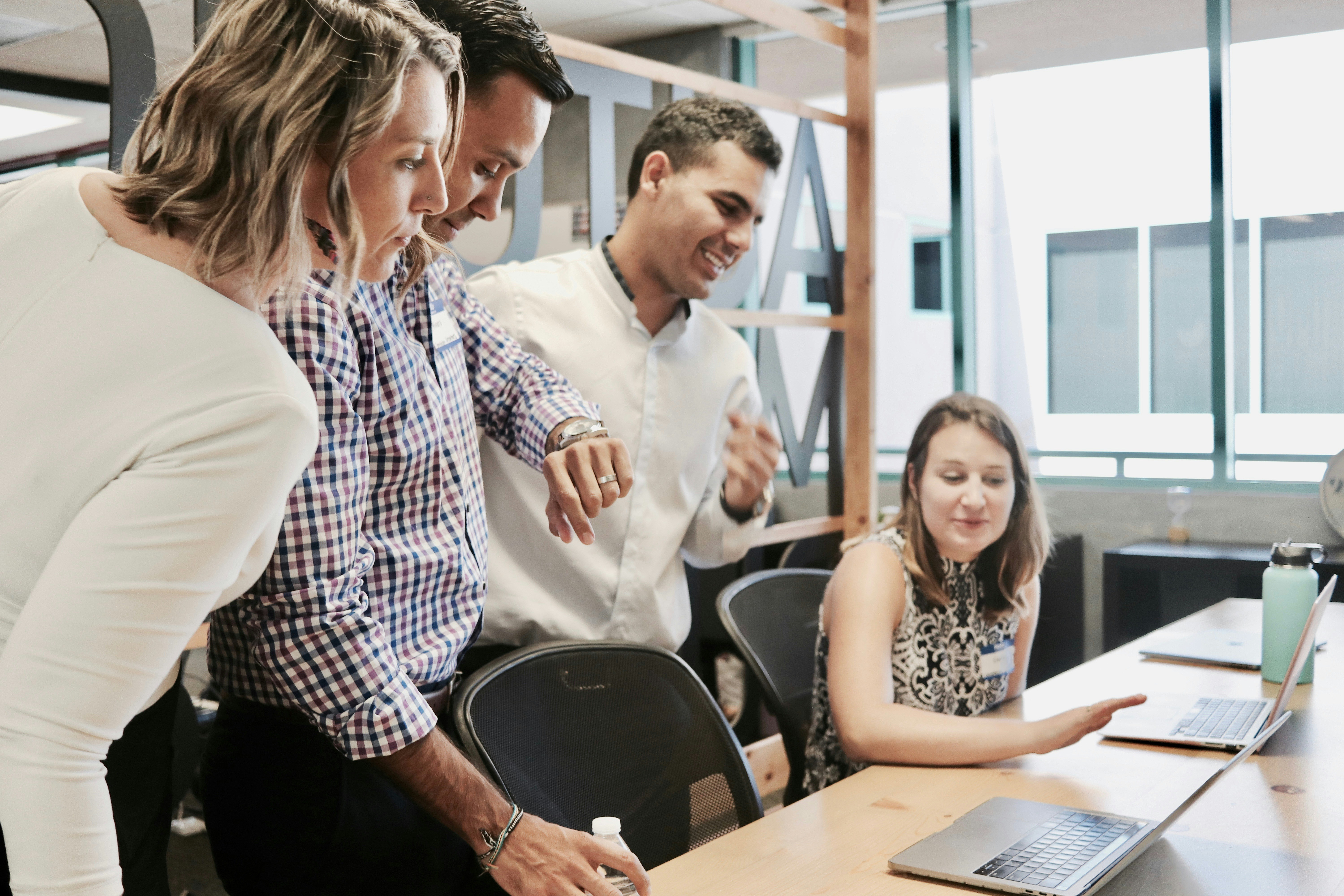 ALT= Debt Recovery Agency + four people standing at a desk + talking + laptops on table + in office building