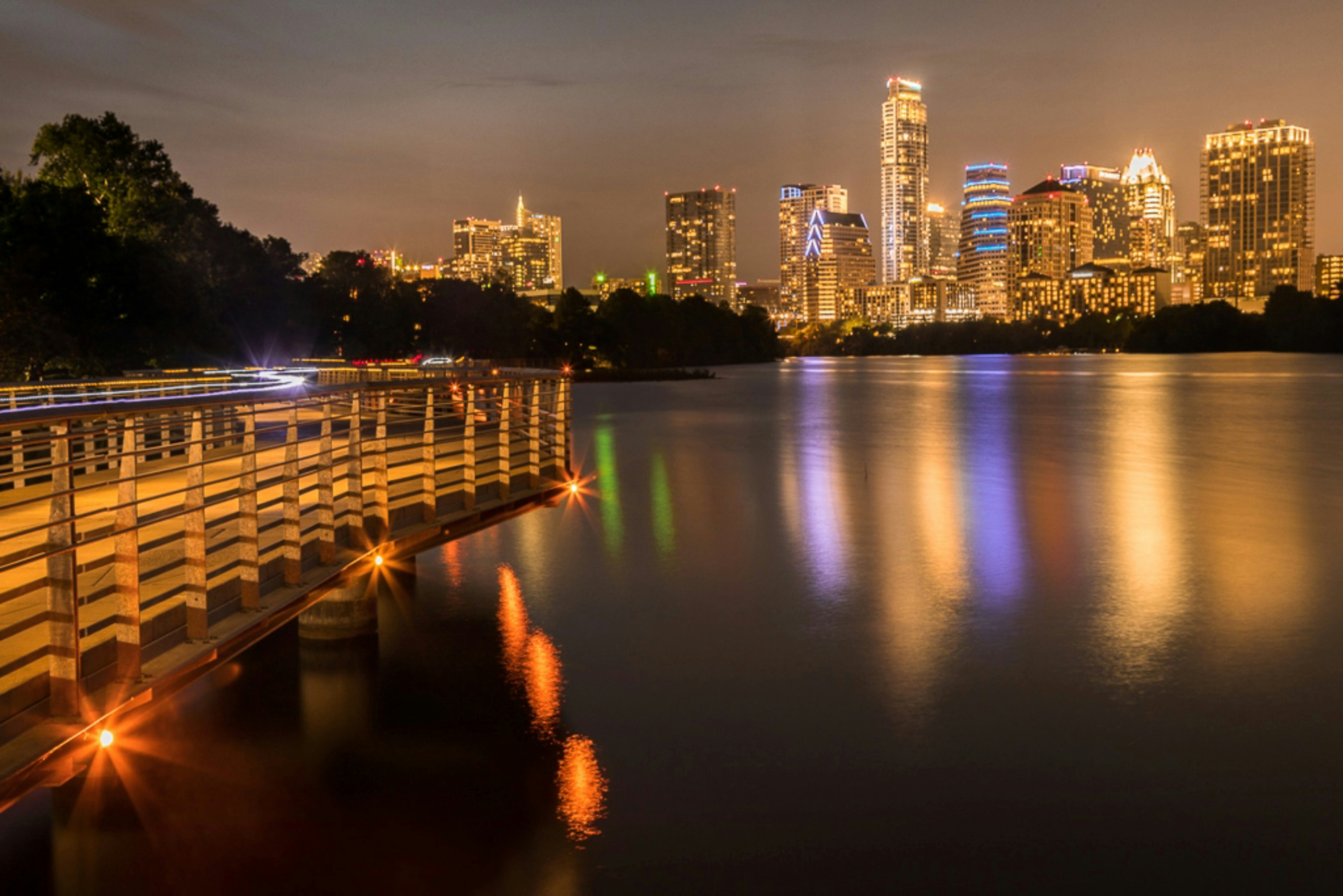 ALT= Debt Collection Agency Austin Texas + night picture of Austin Texas + water + buildings lit up + lights reflecting off water
