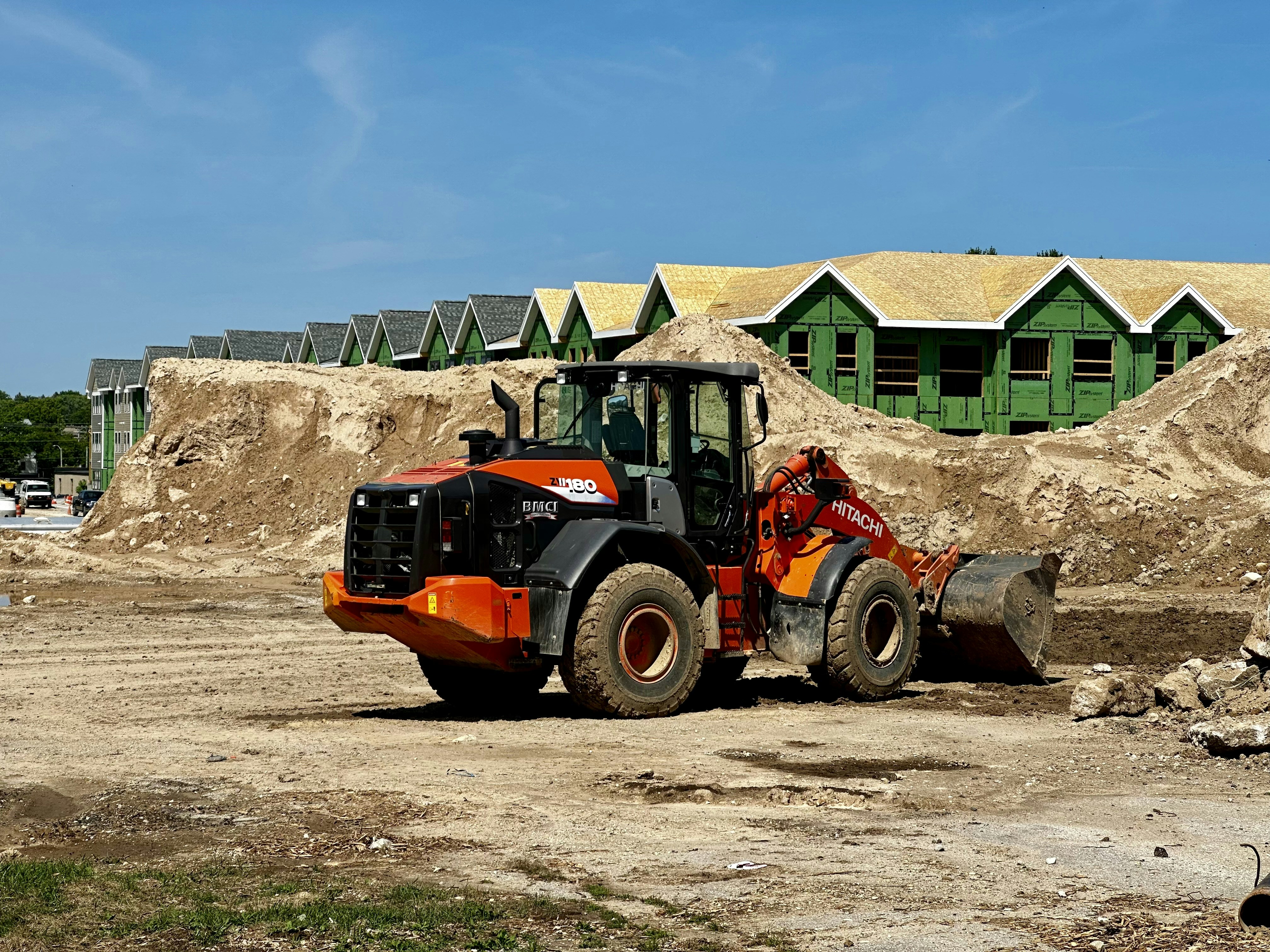black and orange construction equipment on a jobsite with dirt and houses being built in the background