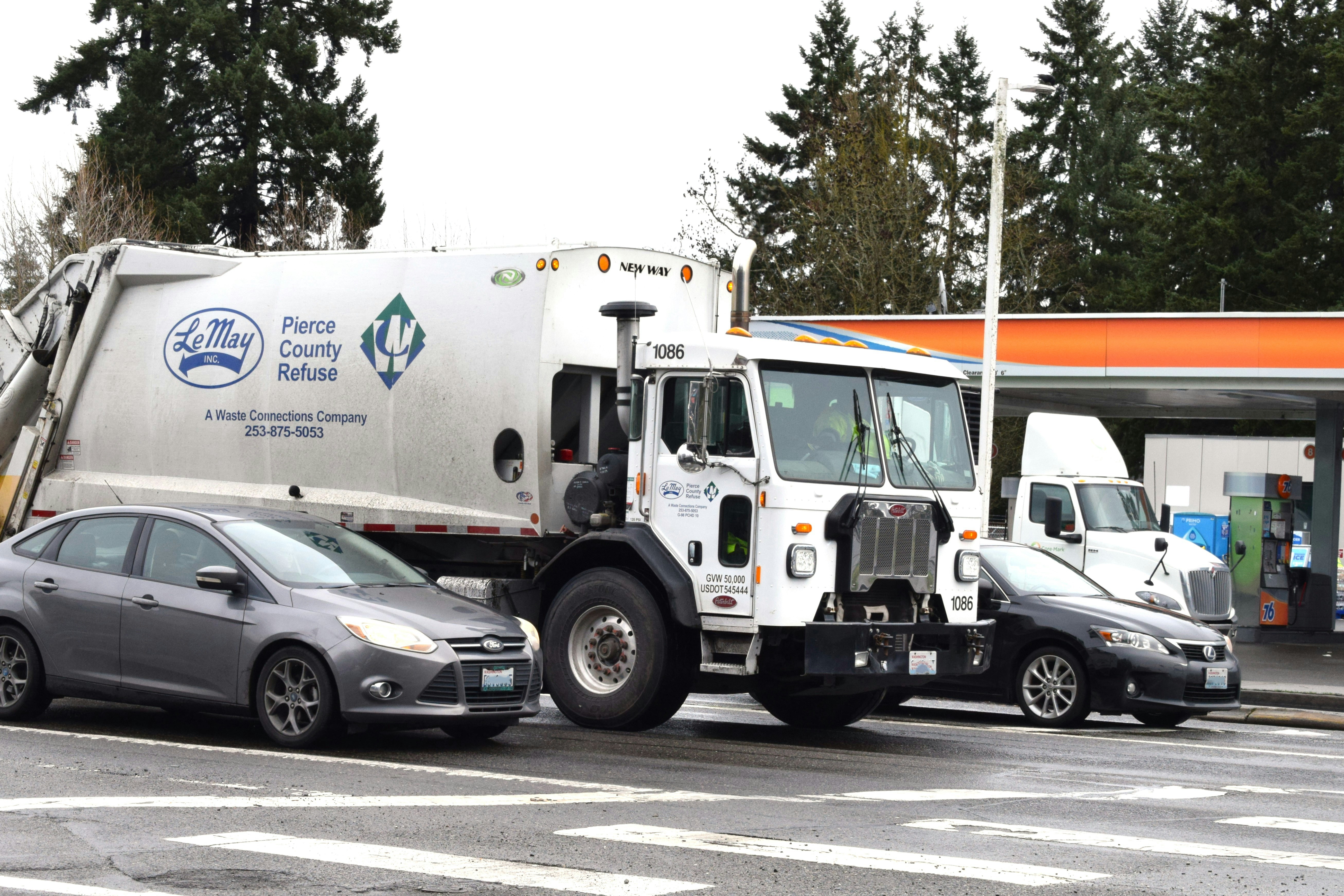 big white garbage truck sitting at a red light in traffice