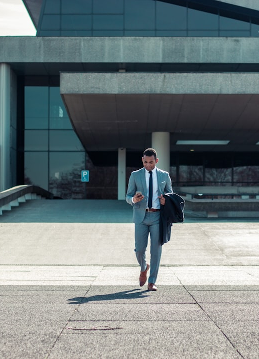 ALT= Hire Debt Collection Agency for Small Business + picture + man walking out of an office building + in suit + on his phone + holding jacket